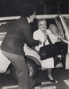 A female volunteer assists an older woman out of the car