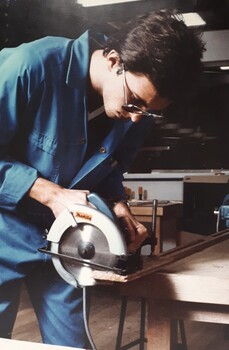 Man in blue coveralls uses a circular saw on a piece of wood