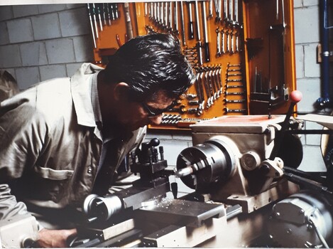 A man in beige coveralls uses a machine in a workshop