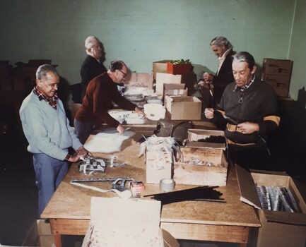 Five men standing around a table packing unknown materials into plastic pockets