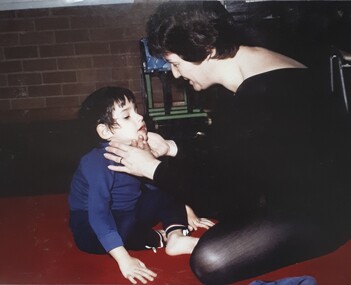 A female teacher gently holds the chin of a young boy