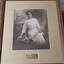 Sepia photograph of woman in early 20th century dress on bench next to flowers and with open book in her lap