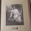 Sepia photograph of woman in early 20th century dress on bench next to flowers and with open book in her lap