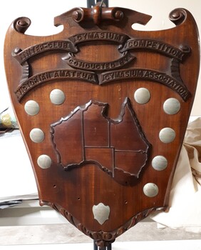 Wooden shield with metal plates and raised wooden map of Australia with state boarders but without Tasmania or the ACT.