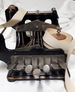 Black metal typewriter which has seven keys and a small reel of paper
