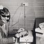 Man smiles and turns towards camera, his fingers poised on a switchboard