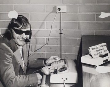 Man smiles and turns towards camera, his fingers poised on a switchboard