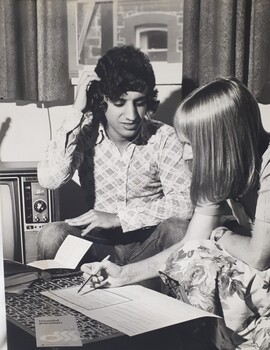 Man speaking to woman in a lounge room with paper forms in front of her