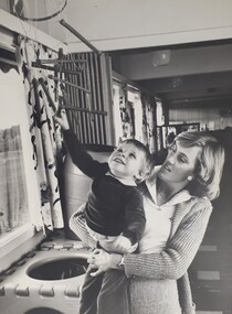 A woman holds a small boy as he reaches for overhanging items