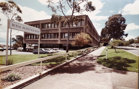 Two storey building on slope, with carpark in front and driveway up to building entrance