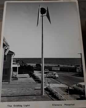 Side view of tall pole topped with a large globe surrounded by metal pieces, overlooking the foreshore at Brighton during the day.
