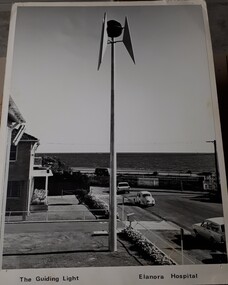 Side view of tall pole topped with a large globe surrounded by metal pieces, overlooking the foreshore at Brighton during the day.
