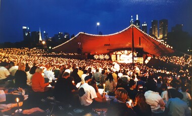 Crowds holding candles and watching an outdoor stage