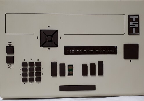Tan coloured rectangle with Braille display and dark brown buttons