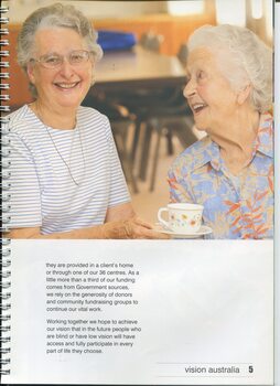 Two older woman chat in a day centre, one holding out a cup of tea to another