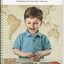 Picture of small boy smiling as he touches tactile boxes which lie next to a Brailled picture book