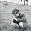 Photograph of small boy kneeling in grass below Burwood building, holding flowers