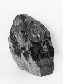 Black and white image of stone block with raised bronze hands and Braille label
