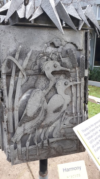 Two pelicans amongst reeds depicting Harmony with a small yellow and blue sign with 'Harmony' written and Braille
