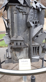 A factory with chimney blowing smoke and a white and black sign with 'Industry' in writing and Braille
