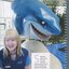 Stephanie Bradbury sitting next to a shark statue at the swimming complex she works at