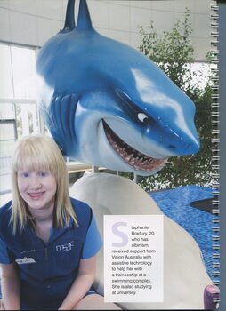 Stephanie Bradbury sitting next to a shark statue at the swimming complex she works at