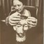 A seated woman touches a sculpture of head, before which rests a sign 'Please do not touch exhibits'
