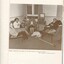 Four people sit in a lounge area, one lady knits whilst two ladies and a man listen to talking books.  Second man kneels at record player.