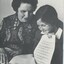 Woman reading Braille music score in her lap whilst a schoolgirl holding a printed score looks on