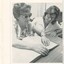 Woman sits at a table reading Braille whilst another looks on