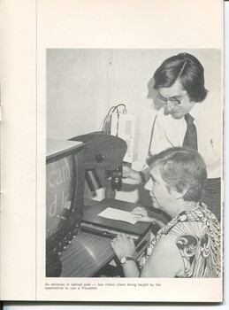 Woman moves a board with paper on it as she watches a CCTV, whilst a man adjusts the lens.
