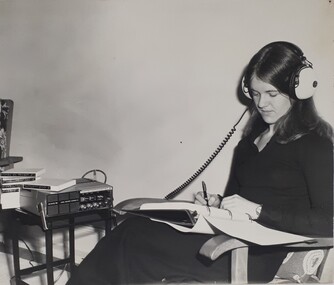 Woman writing in a folder as she listens via headphones to audio reels
