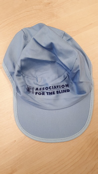 Blue cap with 'Association for the Blind' in navy writing and green on underside of front visor.