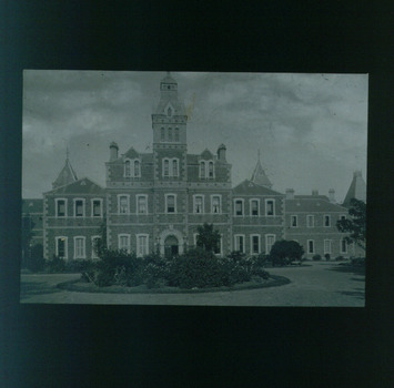 Front of three storey building with circular garden bed filled with bushes and grass