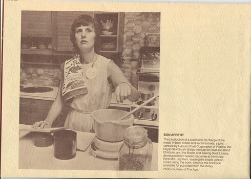 Joy Kerr stands in a kitchen, one hand reading a Braille recipe book and other about to drop something into a bowl