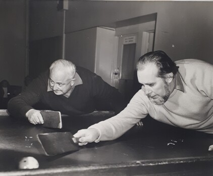 Two men holding bats leaning over a swish table