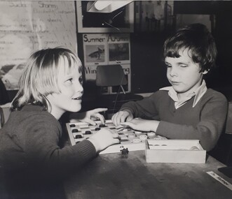 Two children play checkers in a school room