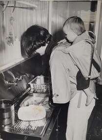 Woman washing dishes whilst holding a toddler on her back