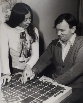 Seated man pressing buttons on machine with lady guiding his hand