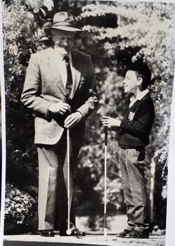 Older man in suit and hat smiles as he stands beside a smiling schoolboy