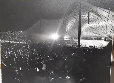 Lighted stage at night, taken from outer stage left over crowds