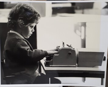 Young boy sits at a table using a Perkins brailler