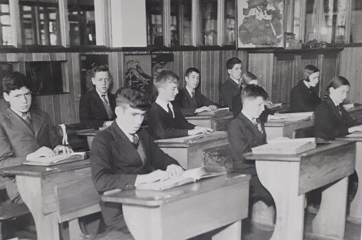 10 pupils sit at wooden desks in their classroom