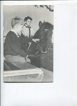 One boy on a pony whilst another pats it