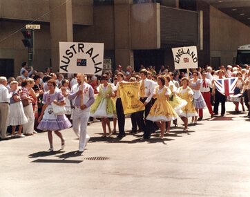 Square dance troupe walking through street behind 'Australia' sign