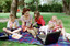 Sigrid and five children sit on picnic blanket as she reads a story, with two open suitcases beside them