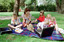 Sigrid and five children sit on picnic blanket as she reads a story, with two open suitcases beside them