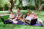 Sigrid and five children sit on picnic blanket as she reads a story, with two open suitcases beside them