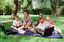 Sigrid and five children sit on picnic blanket as she reads a story, with two open suitcases beside them