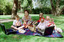 Sigrid and five children sit on picnic blanket as she reads a story, with two open suitcases beside them